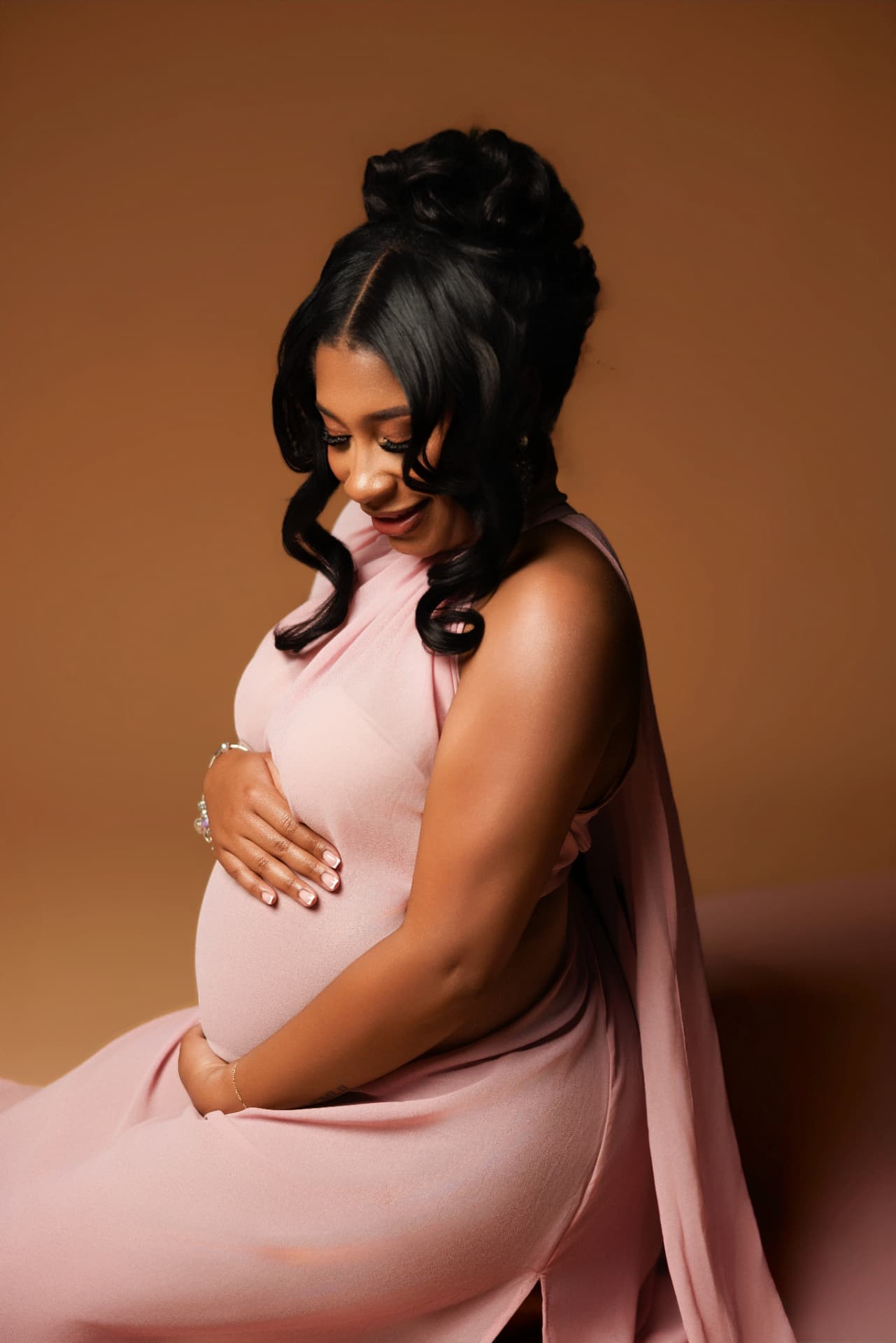 Expectant mother in a blush gown cradling her bump
