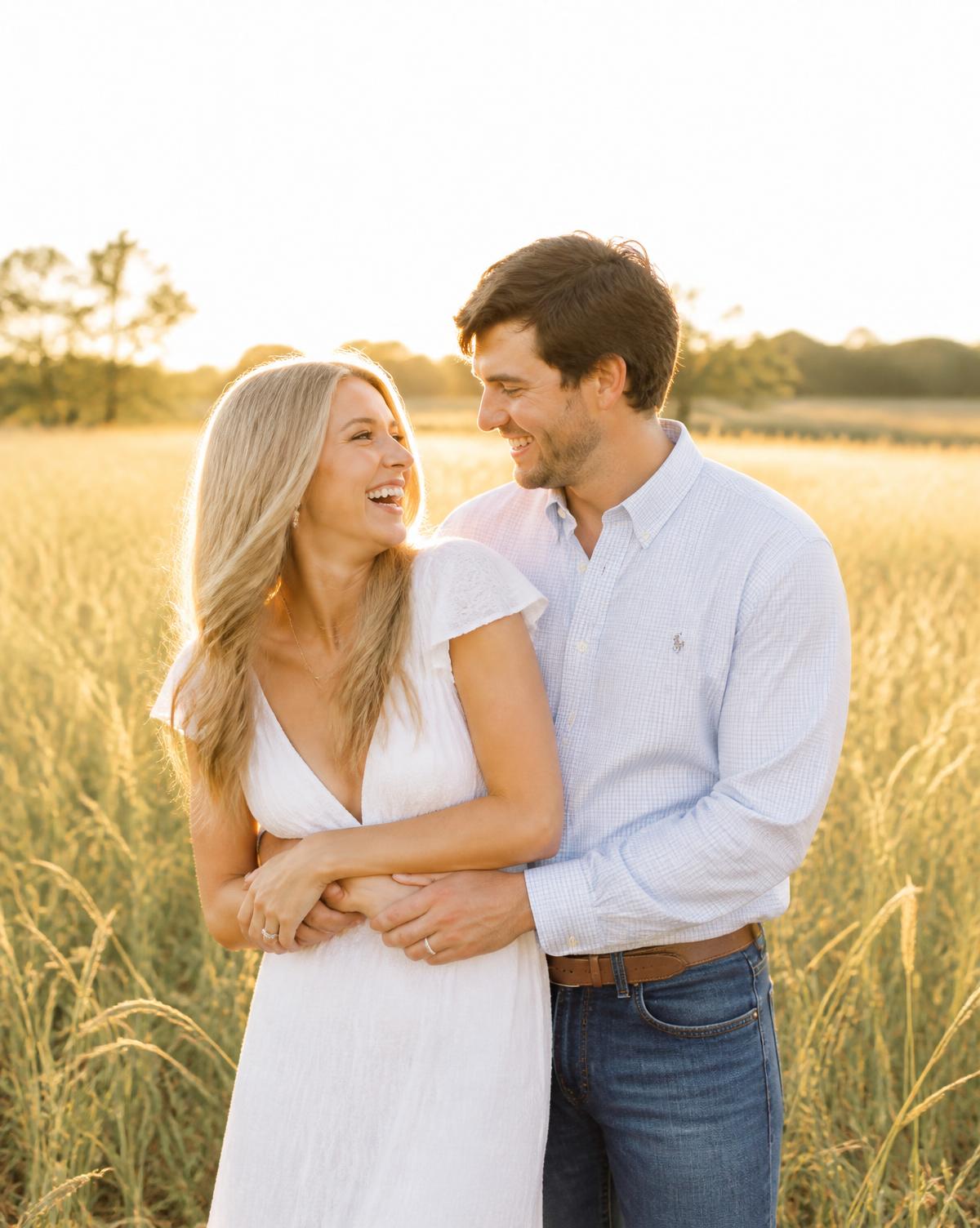 Engaged couple laughing together in a sunlit field at golden hour