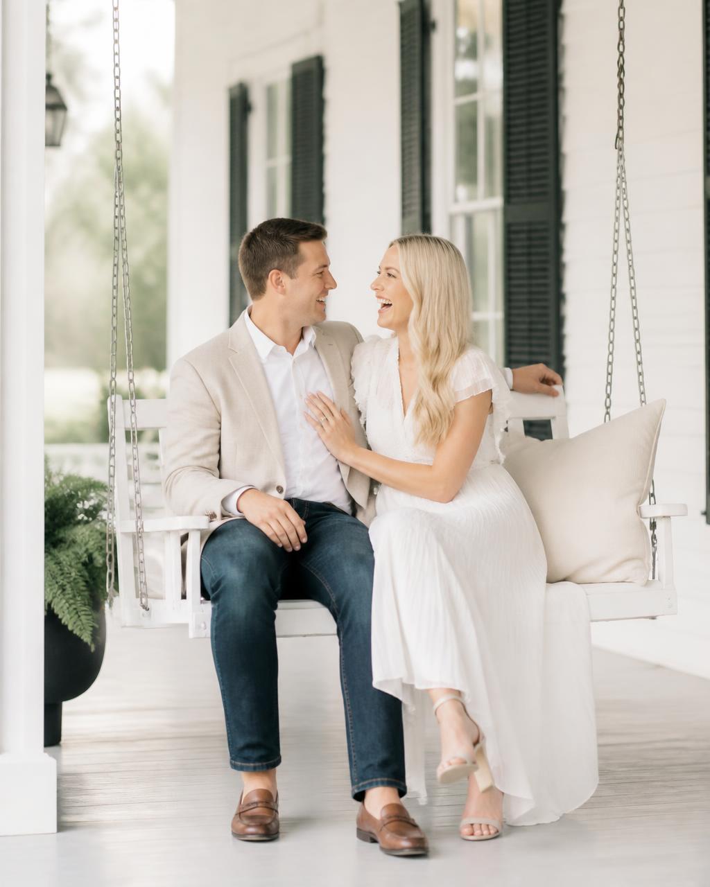 Couple laughing on the porch swing of a white farmhouse