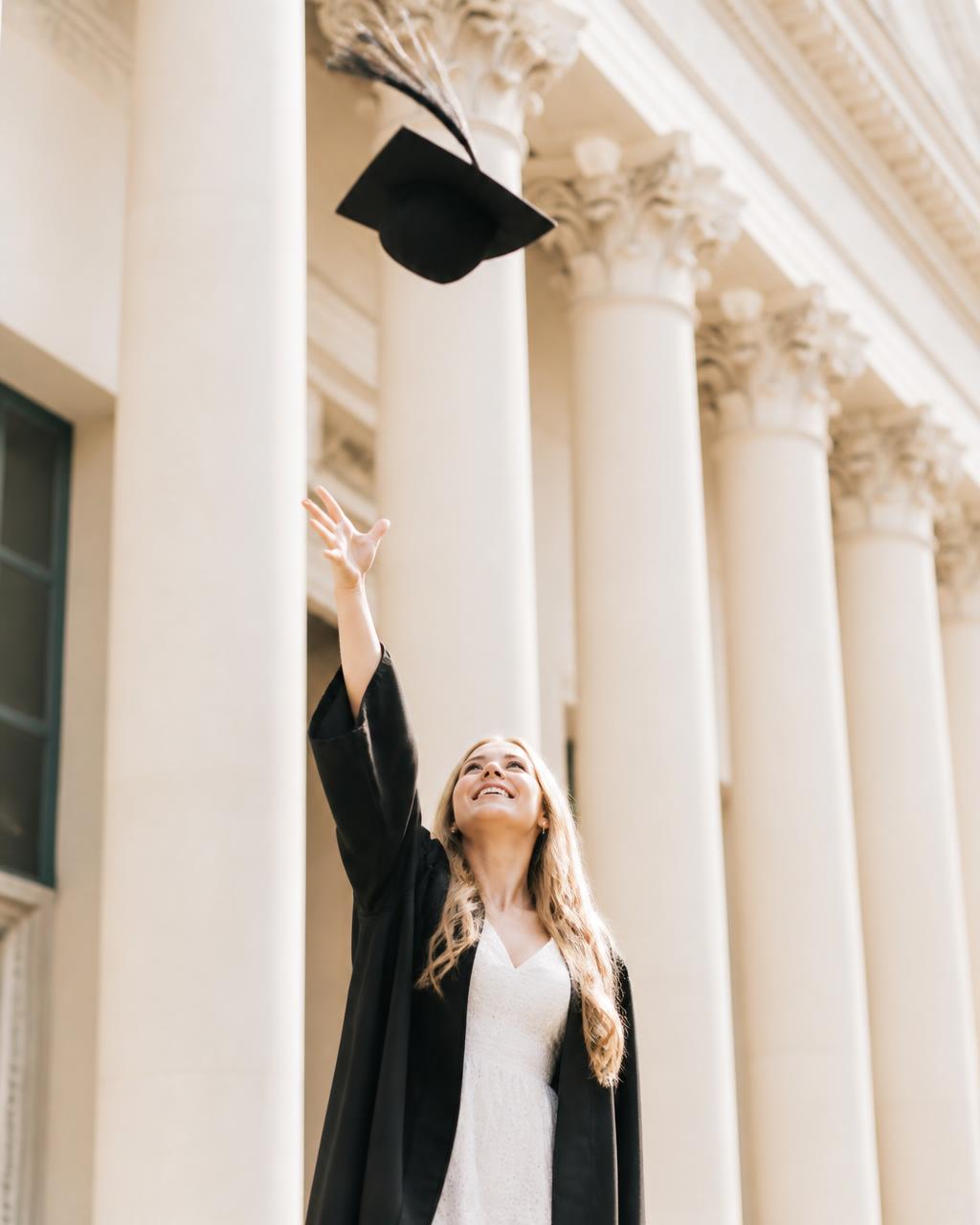 Graduate tossing her cap in front of campus columns