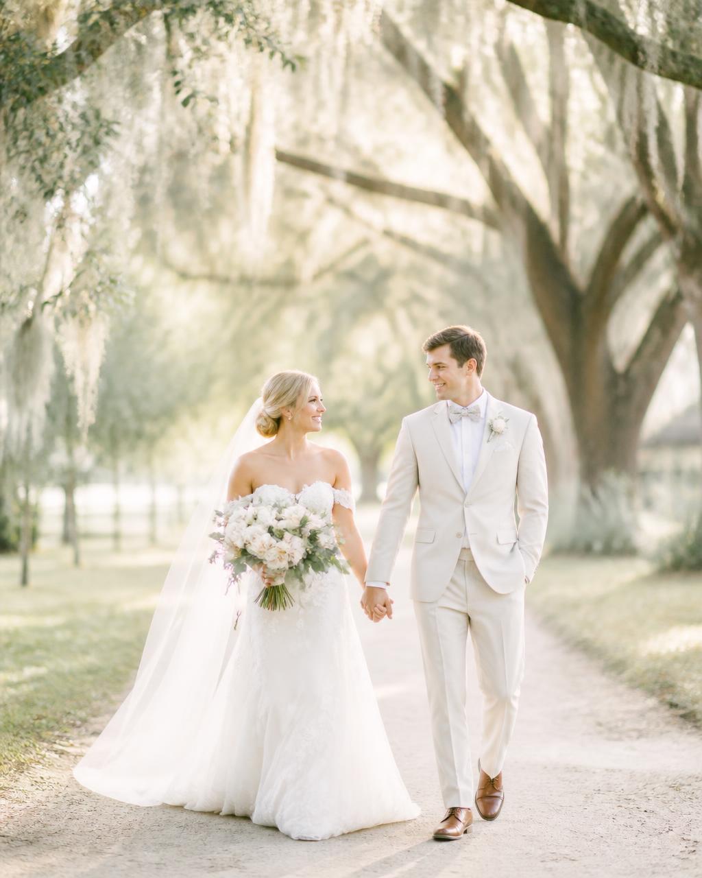 Malachi and Ana walking hand in hand beneath moss-draped oaks