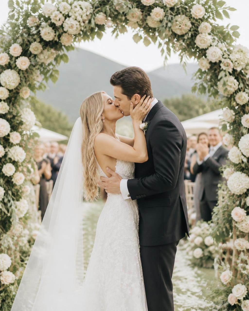 First kiss at the outdoor ceremony beneath a floral arch